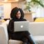 An African American woman working remotely on a laptop in a modern indoor setting.